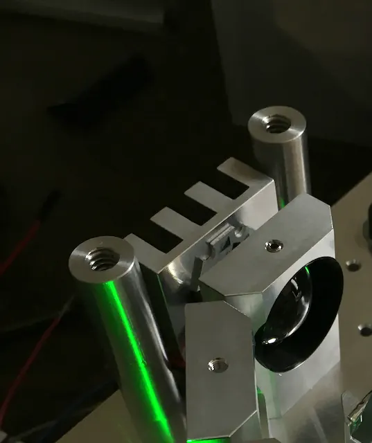 A machined aluminum heat-sink block with a green laser line