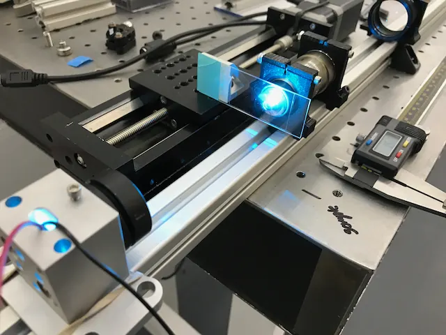 An optical rail with a blue-lit cube mount and a digital caliper