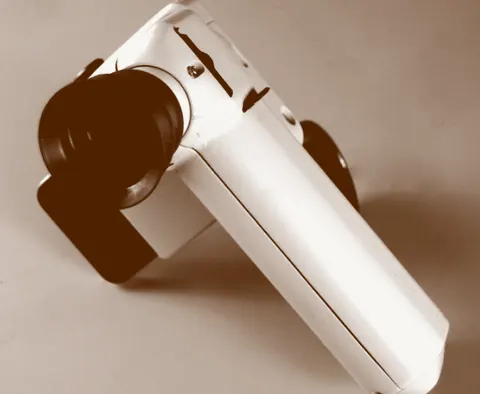 A white handheld instrument housing with a dark lens port