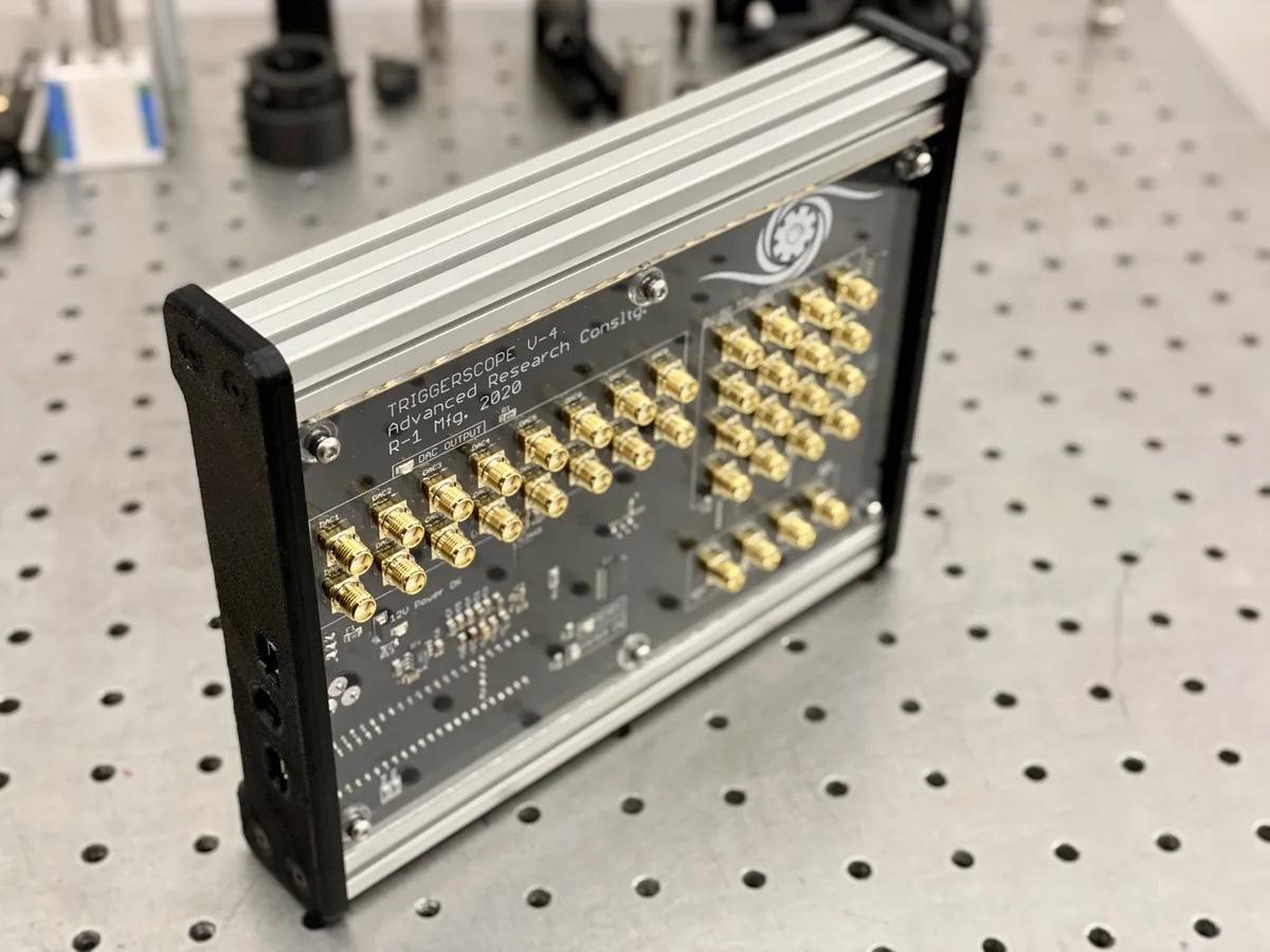 Triggerscope 4 on an optical breadboard, rows of gold SMA connectors on a black panel